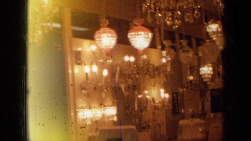 The frame shows a London lighting or antique showroom interior with chandeliers, wall sconces, crystal drops, and amber 8mm color.