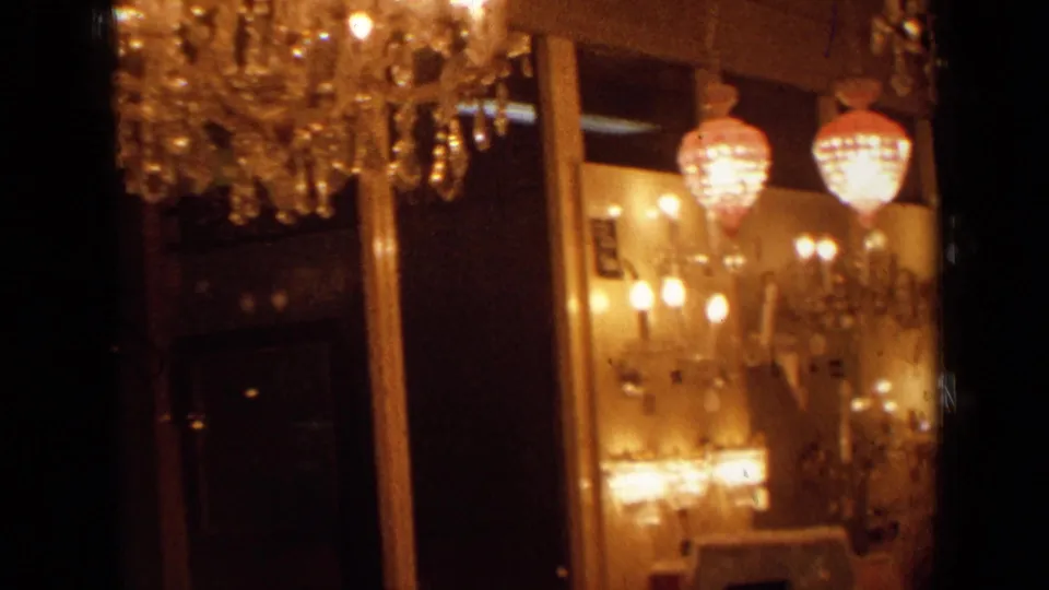 A closer 8mm view shows crystal chandelier details, glowing wall lamps, hanging globe fixtures, and reflective surfaces in the 1963 London setting.