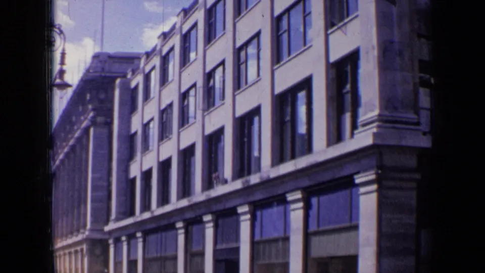 A panning 1963 London street shot frames the building facade with repeated windows, columns, and a decorative lamp post.