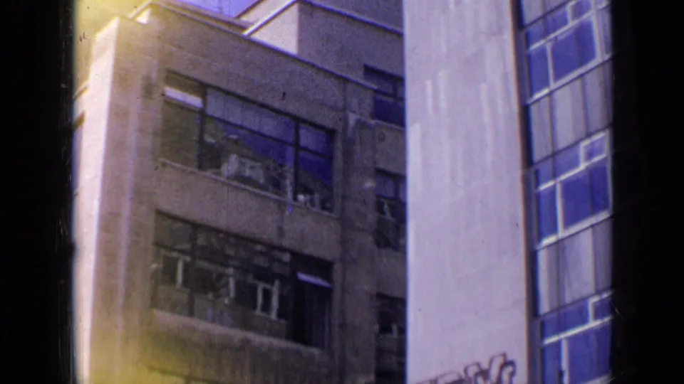 1963 London 8mm frame with a closer view of a weathered multi-story facade, broken windows, and a pale neighboring wall.