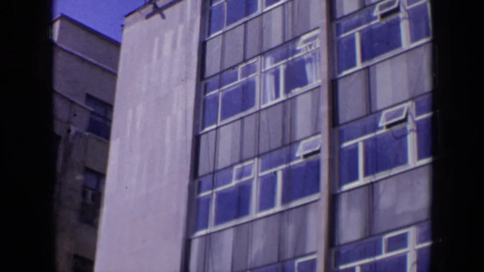 1963 London 8mm frame showing a tall modern building facade with blue-tinted windows and white framing.