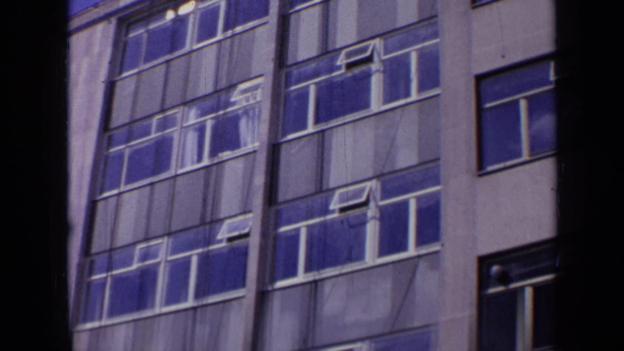 1963 London frame with repeated blue reflective windows, white mullions, and pale facade panels on a modern building.
