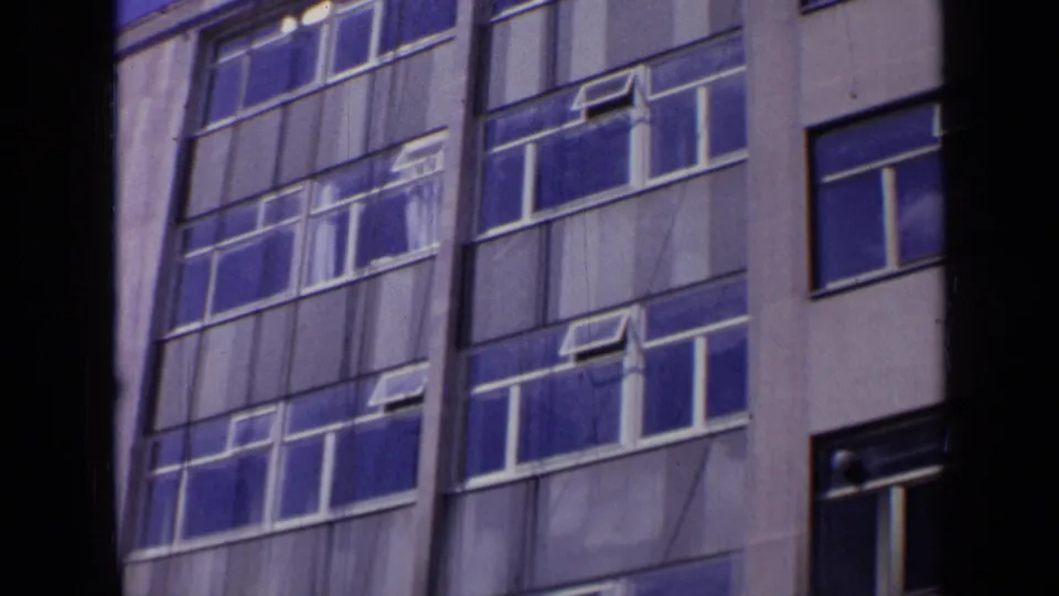 1963 London frame with repeated blue reflective windows, white mullions, and pale facade panels on a modern building.