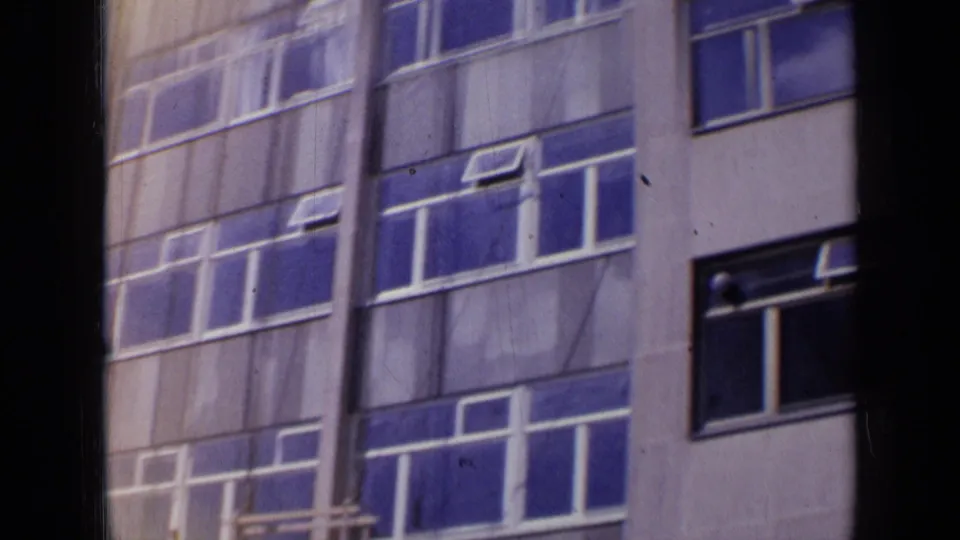 1963 London 8mm frame showing a windowed building exterior with blue panes and a dark foreground obstruction.