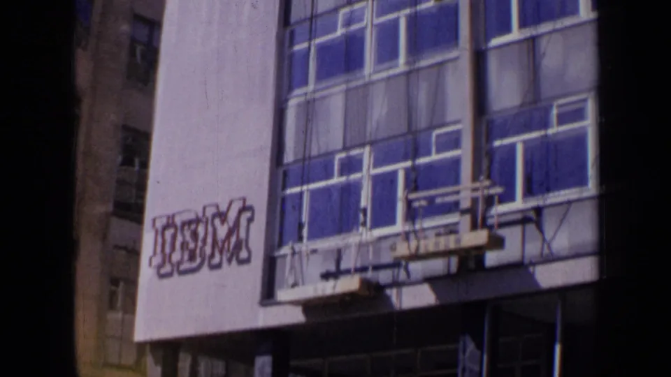 1963 London frame showing a modern building exterior with blue windows, pale panels, and a visible IBM sign.