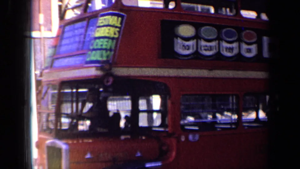 Red London double-decker bus passes close to the camera, with passengers visible and an advertising panel along the upper side.