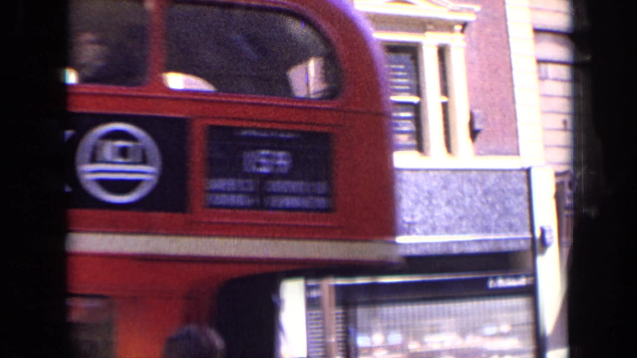 Rear section of a red double-decker bus beside London shopfronts and buildings.