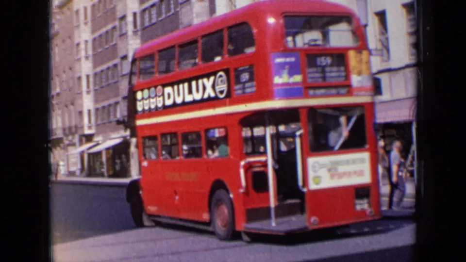 1963 London frame showing a red route 159 double-decker bus with Dulux side advertising, pedestrians and period street buildings.