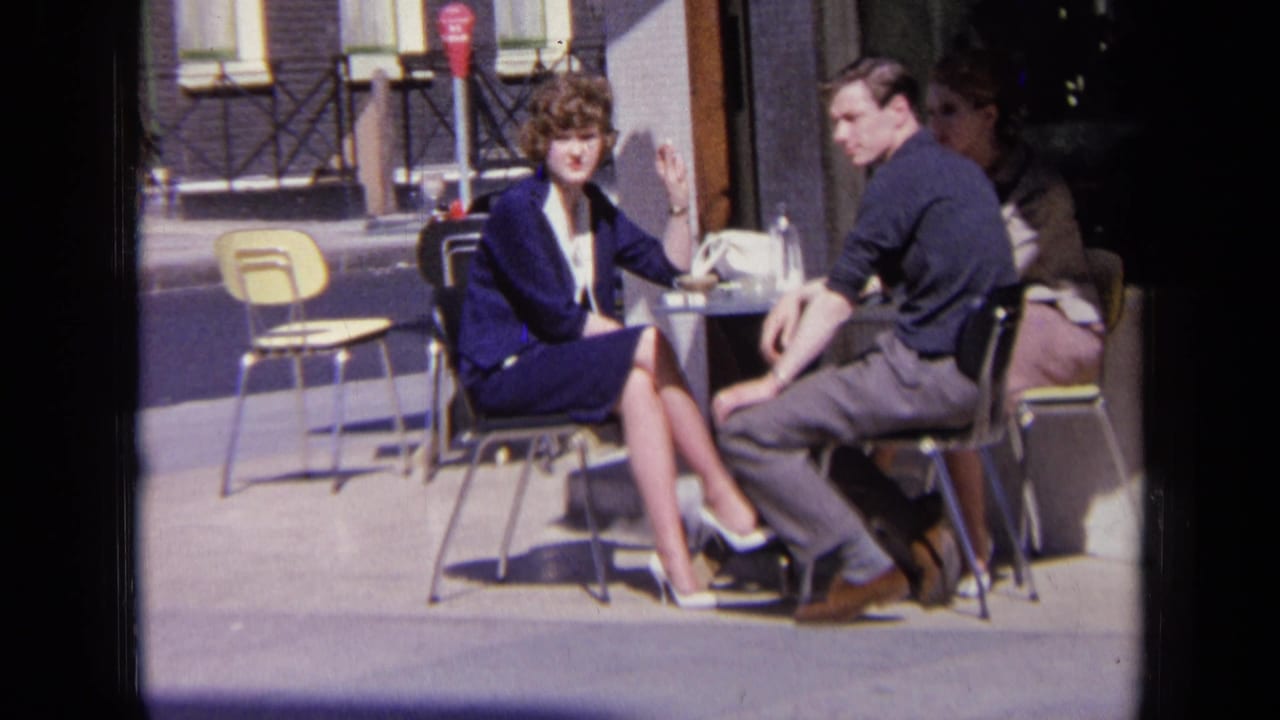 Woman in a blue suit and man in a dark shirt sit at a small outdoor table.