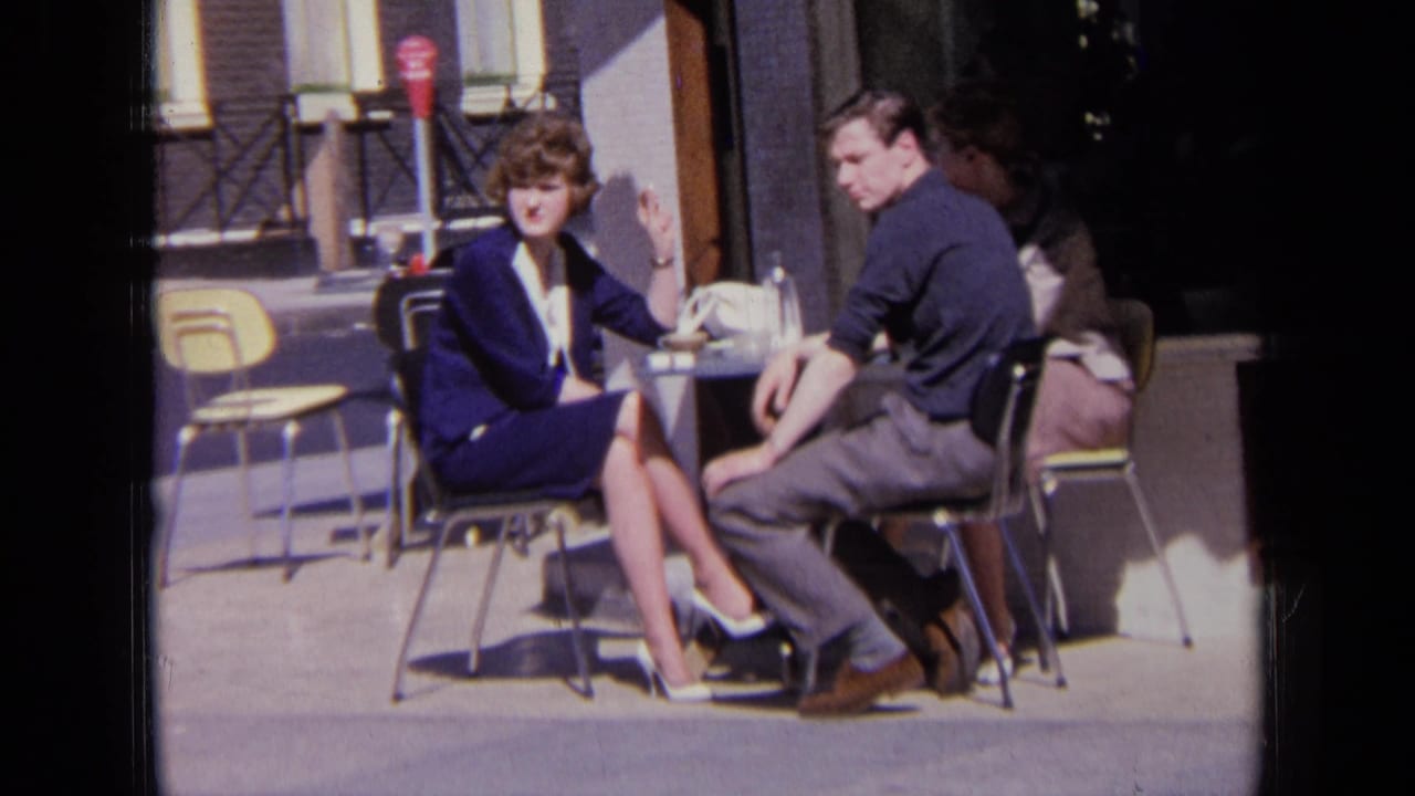 The seated pair glance toward the camera while sitting outside on a London street in 1963.