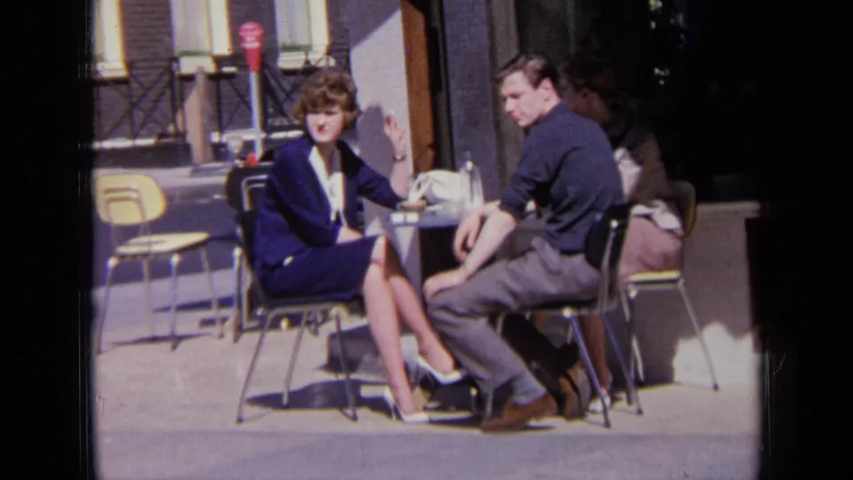 The seated pair glance toward the camera while sitting outside on a London street in 1963.