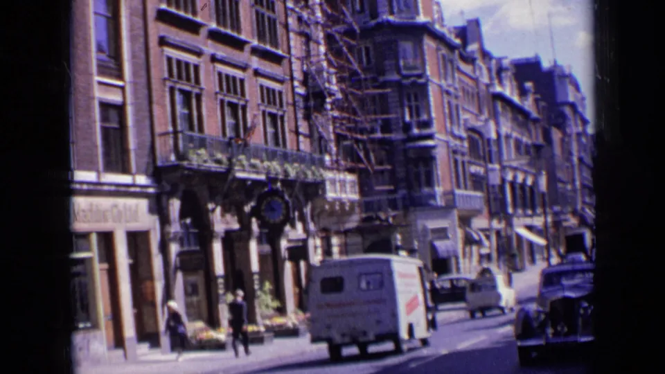 A 1963 London street view shows multi-story shopfronts, scaffolding, pedestrians, a van, and a dark car in traffic.