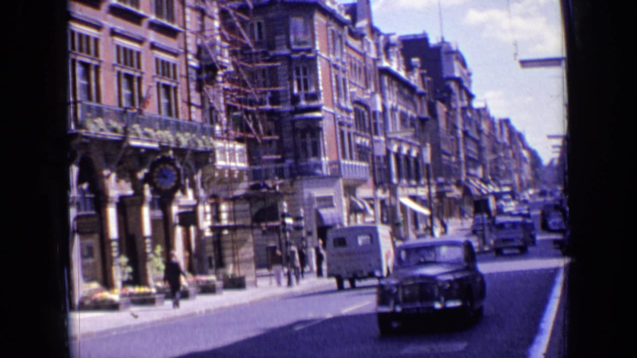 Street view with pedestrians, shopfronts, a white van, and a dark car moving toward camera.