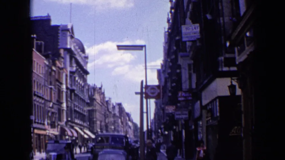 1963 London street view with storefront awnings, pedestrians, vintage cars, tall buildings, and a visible Underground roundel.