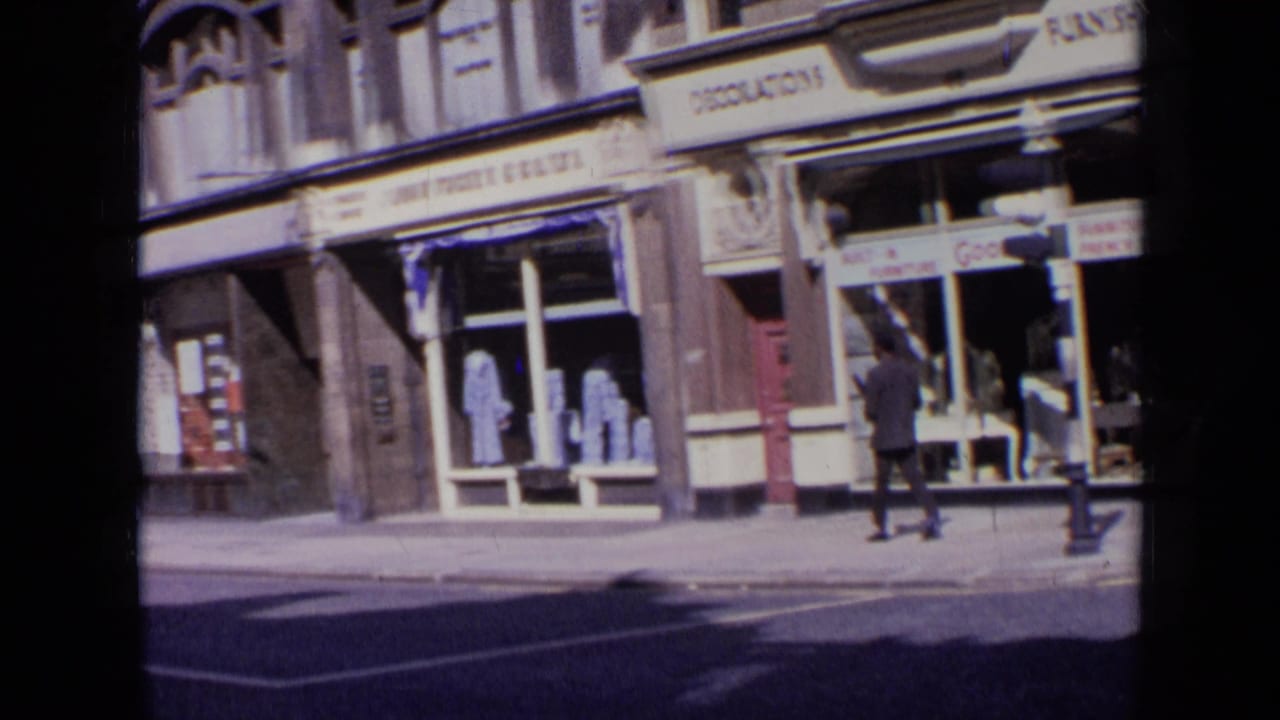 A man walks past storefront windows and signs along a bright city pavement.