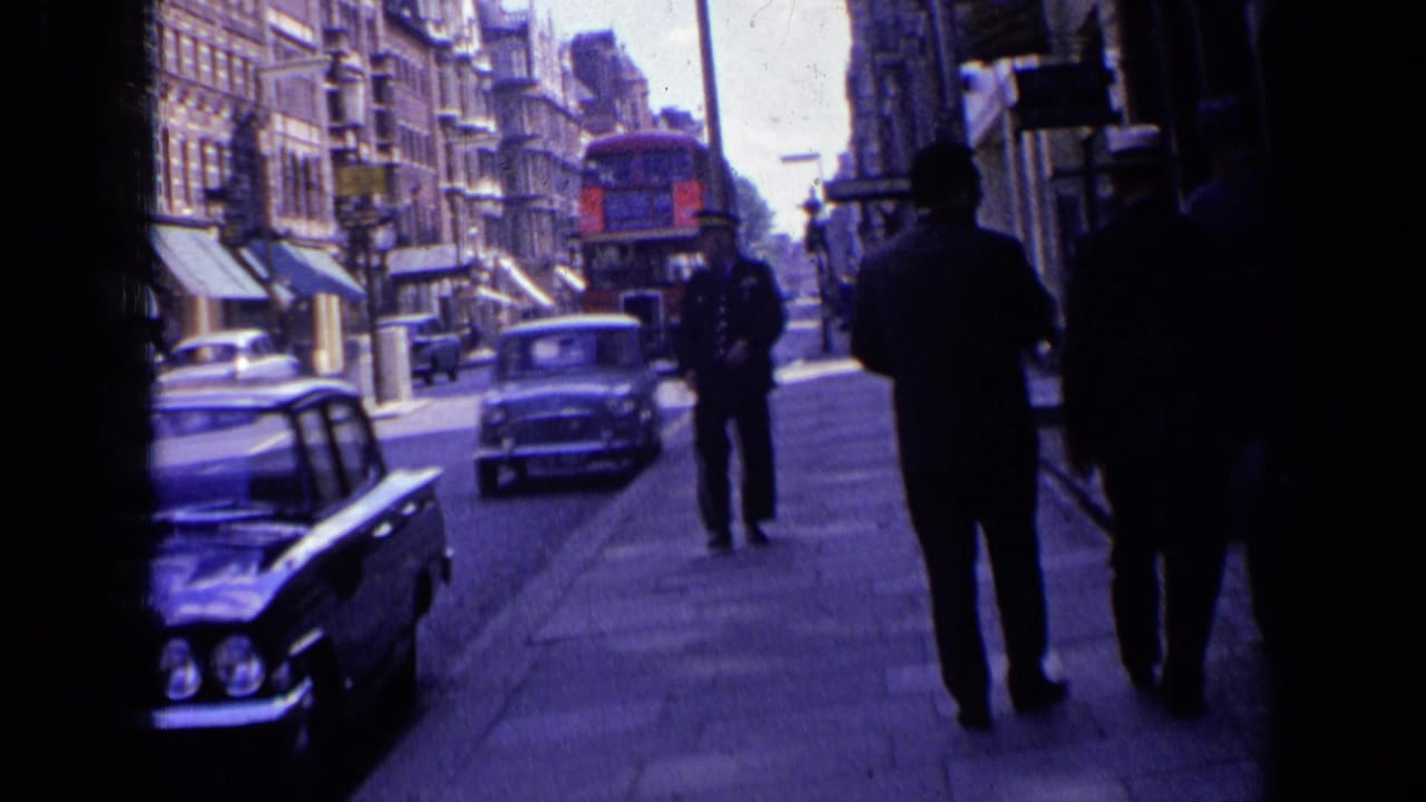 Sidewalk view with a police officer, pedestrians, classic cars, shop awnings, and a red bus ahead.