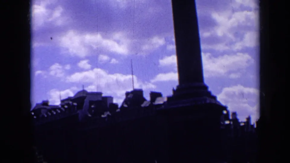 1963 London home-movie frame showing Nelson's Column in silhouette against a purple-tinted sky above Trafalgar Square buildings.