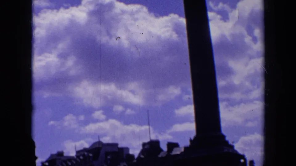 London 8mm frame with Nelson's Column silhouetted over Trafalgar Square, with rooftops and bright clouds behind it.