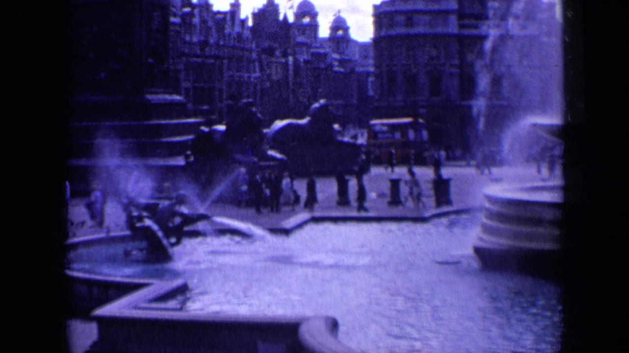 London square with fountain spray, pedestrians, distant traffic and stone buildings.
