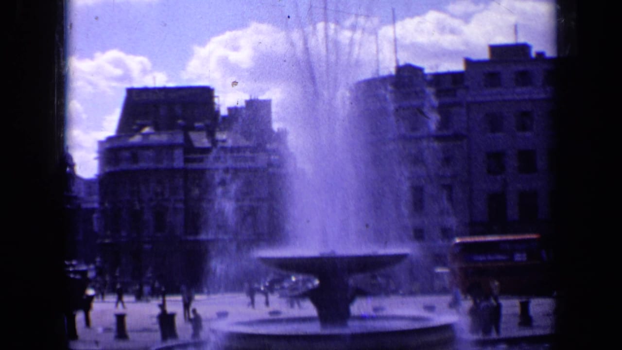 Large stone fountain spraying water in a London square with pedestrians and buildings behind it.
