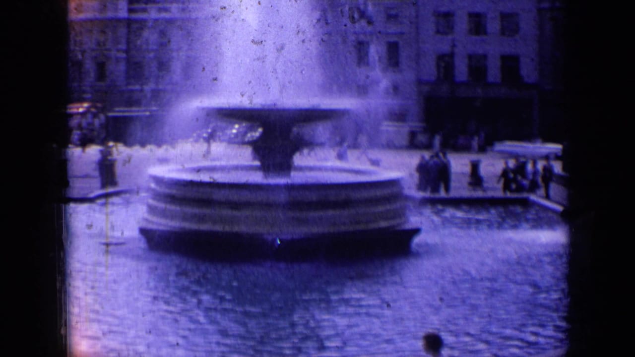 Soft 8mm view of a London fountain basin in 1963, with people along the square and architecture in the background.