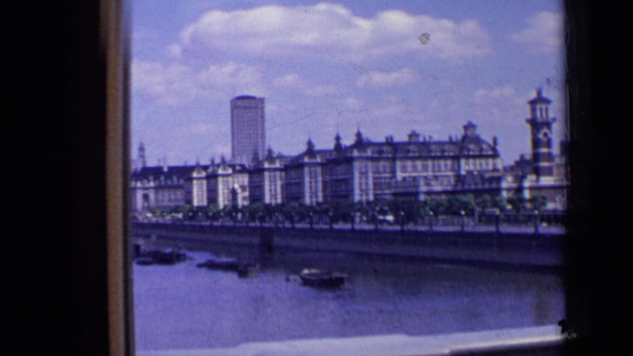 1963 London riverfront skyline with small boats on the river, older buildings along the bank, and a tall modern tower in the background.