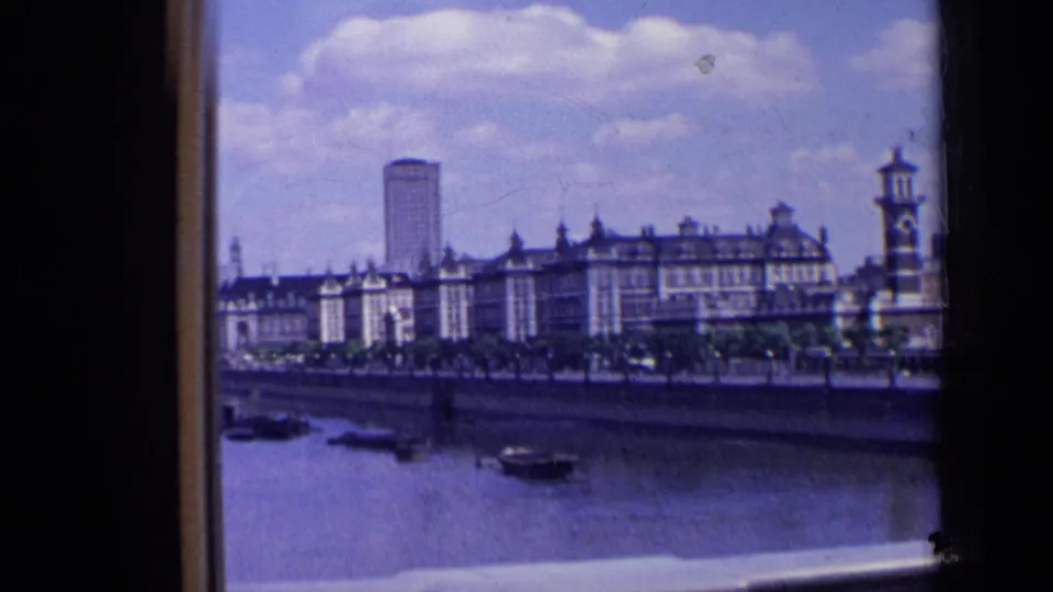 1963 London riverfront skyline with small boats on the river, older buildings along the bank, and a tall modern tower in the background.