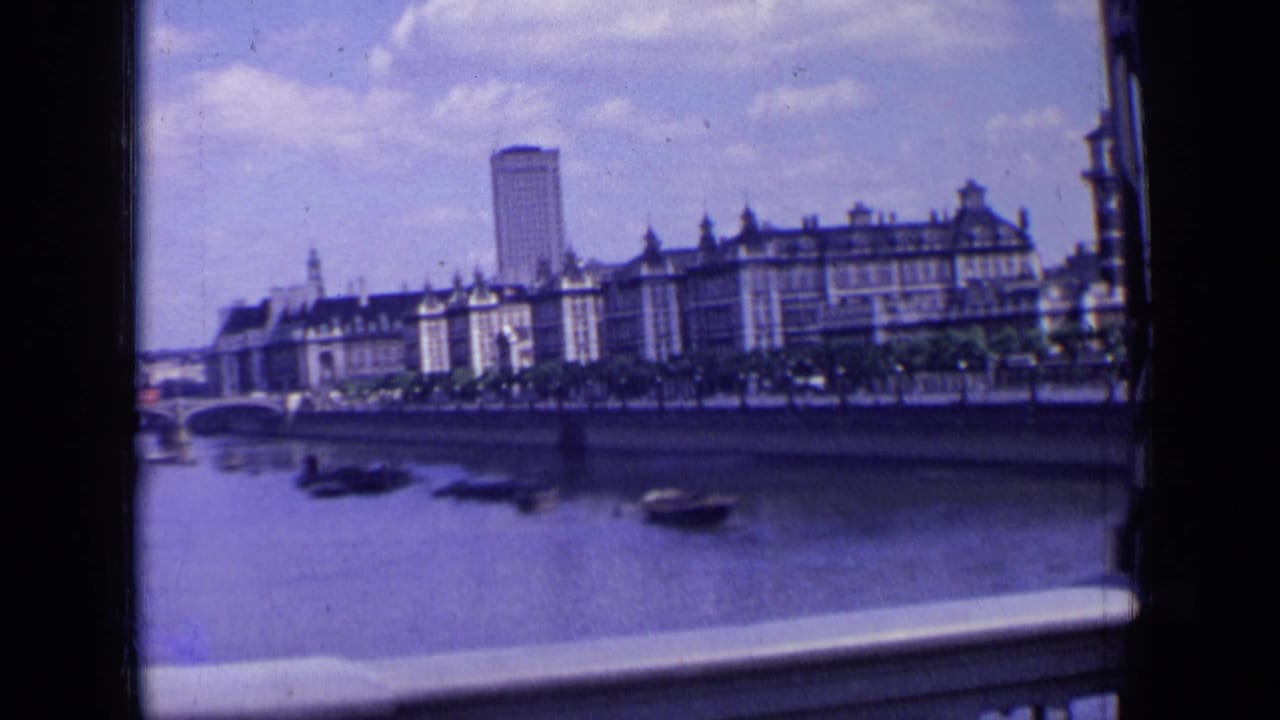 1963 London riverside view during a pan, showing boats on the river, a bridge arch at left, waterfront buildings, and a tall background tower.