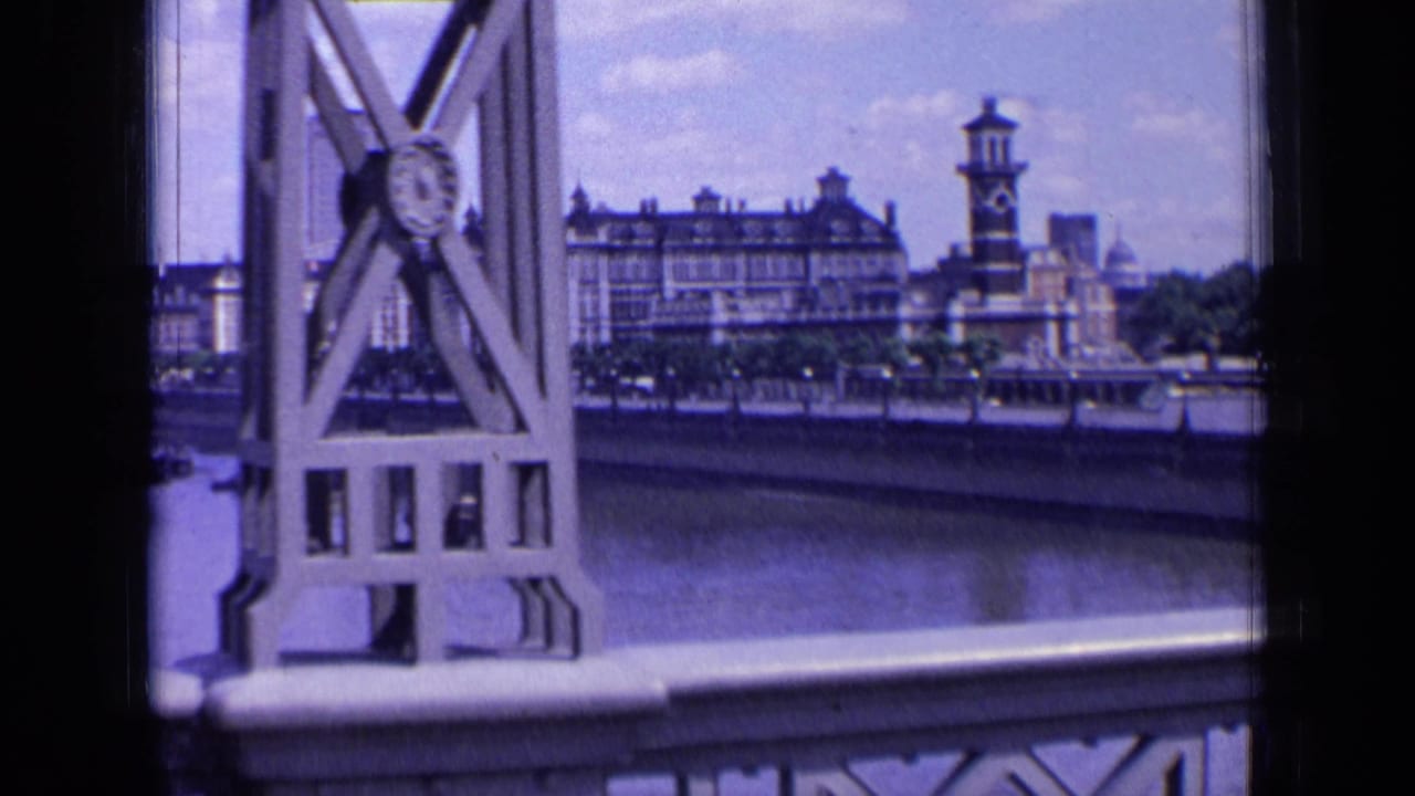 Ornate bridge truss and railing with London riverside buildings across the water.
