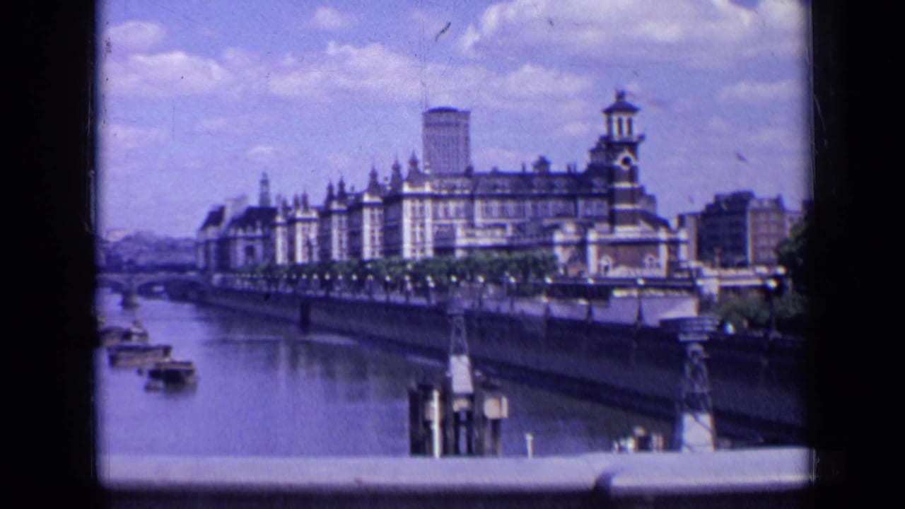 1963 London home-movie frame showing a large ornate building along the river, small boats on the water, and a bridge in the distance.