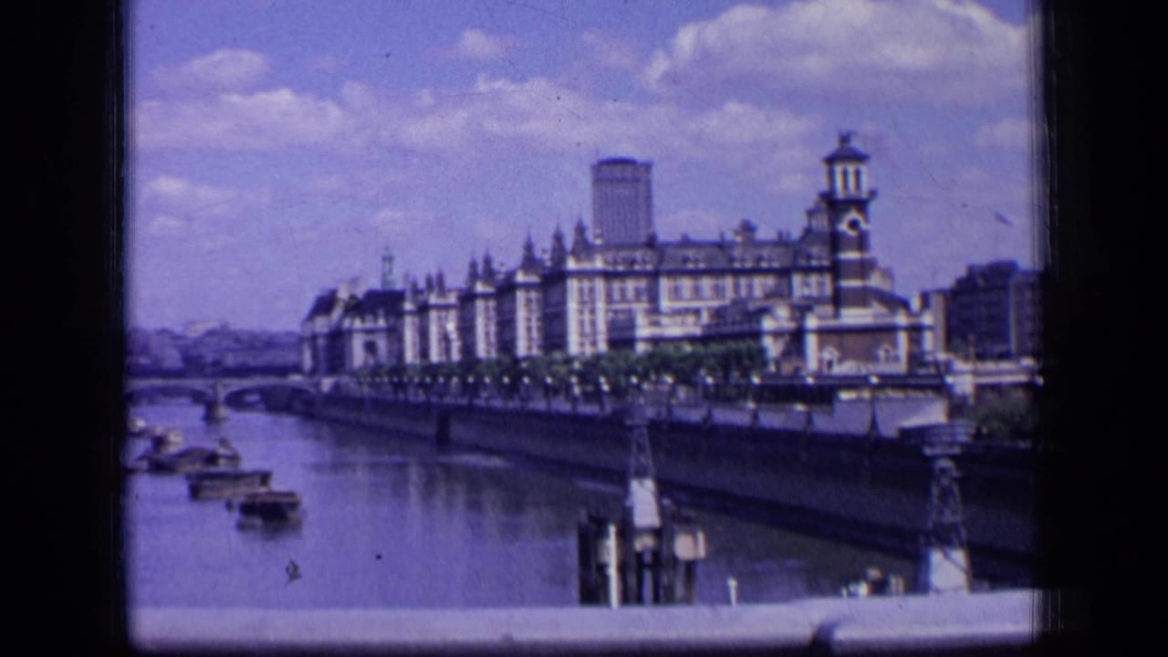 River view with boats, a bridge, and a large riverside building under a cloudy sky.