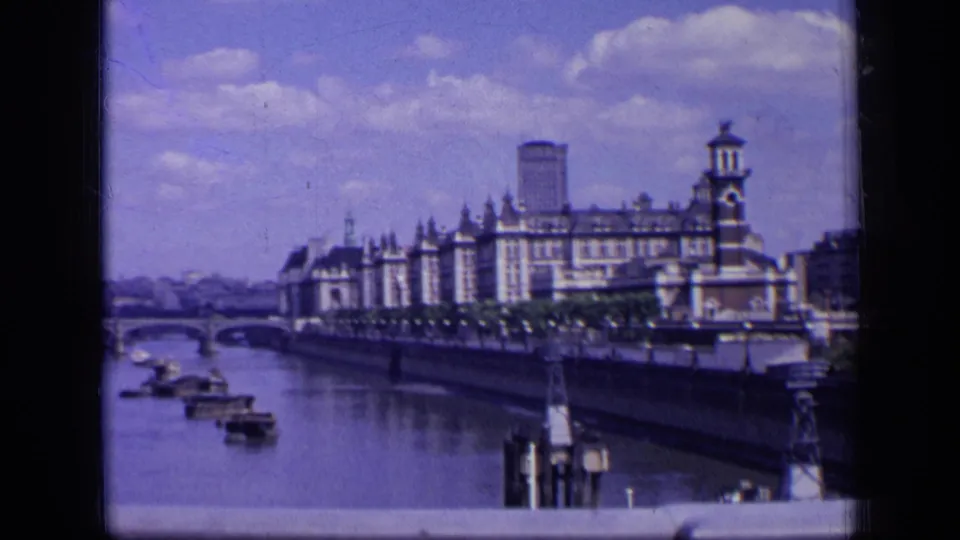 1963 London 8mm frame of the Thames with boats, bridge structure, embankment trees, and a prominent riverside building.