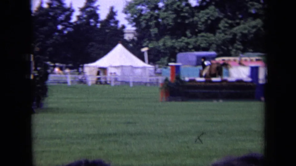 1963 London home-movie frame showing a grassy riverside area with tents, trees, and a moored narrowboat or canal-style vessel.
