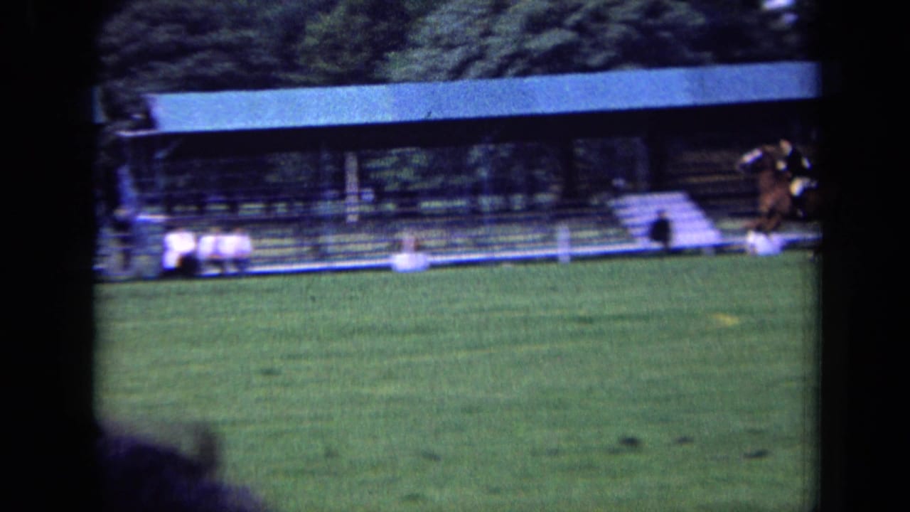 In 1963 London footage, a horse and rider move across a grass equestrian field with spectators seated under a covered stand.