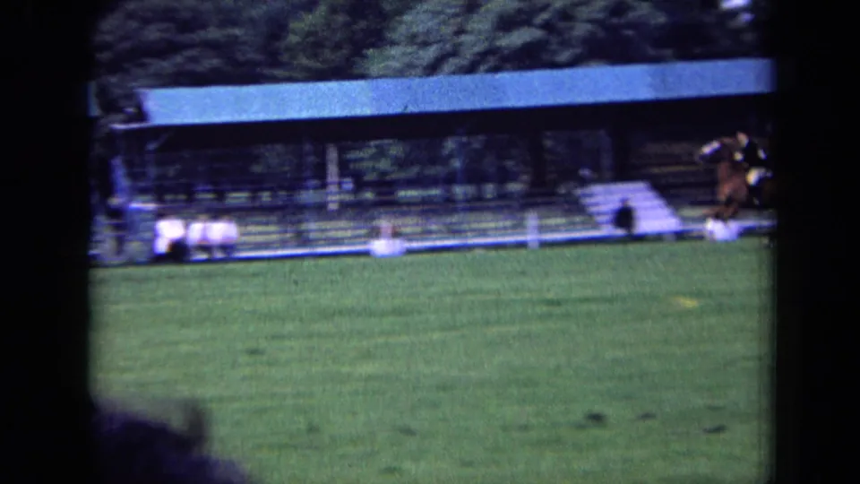 In 1963 London footage, a horse and rider move across a grass equestrian field with spectators seated under a covered stand.