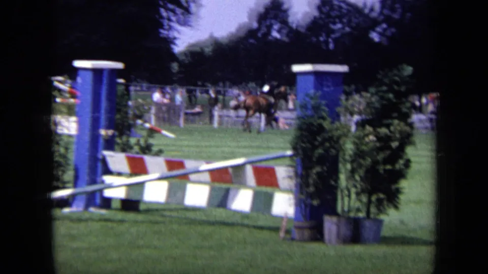 1963 London 8mm frame showing a horse and rider on a grassy show-jumping course with striped rails and potted shrubs.