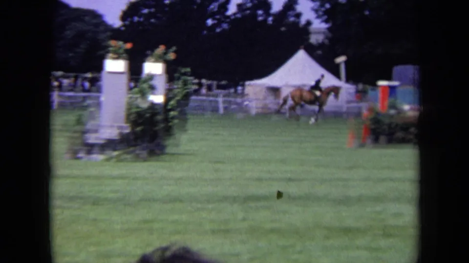 1963 London 8mm frame showing a horse and rider moving past a white obstacle standard with tents behind the course.
