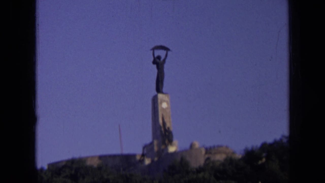 1963 8mm home-movie frame from Russia showing a distant monumental statue above a low structure and treeline.