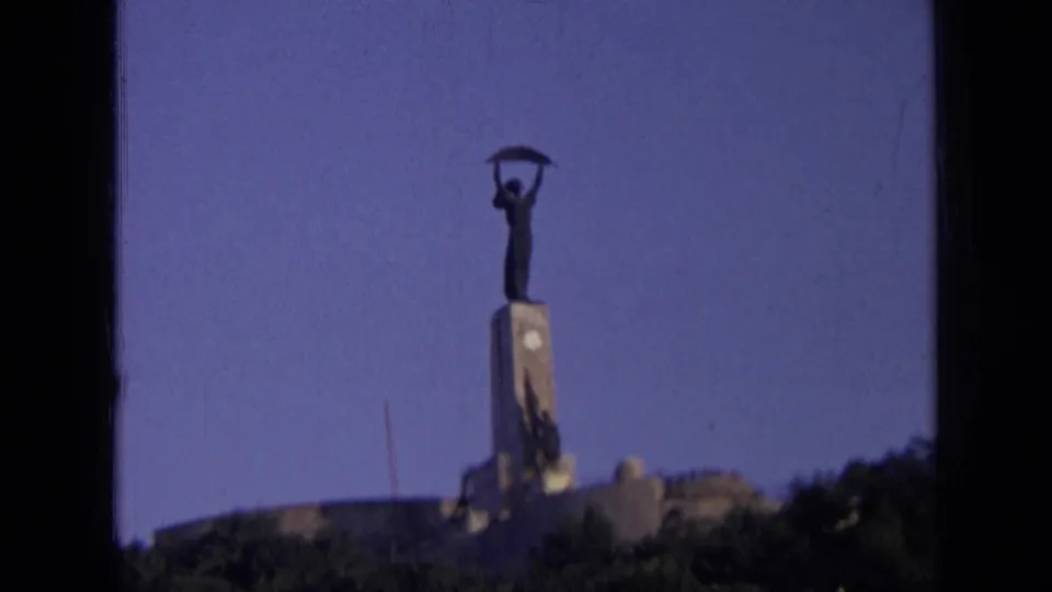 1963 8mm home-movie frame from Russia showing a distant monumental statue above a low structure and treeline.