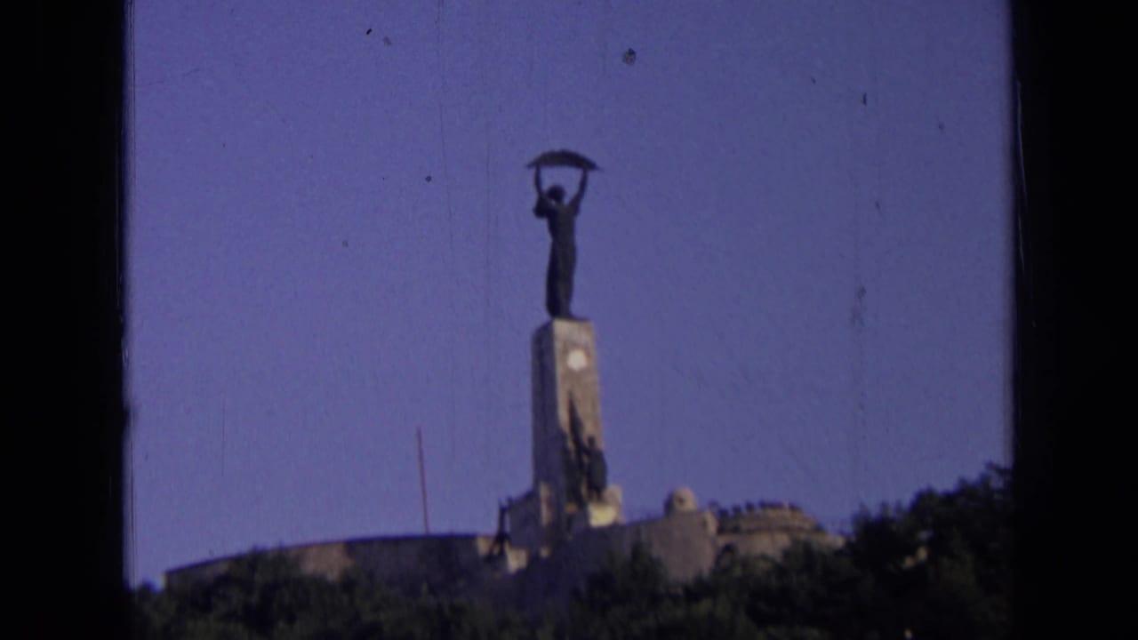Distant Russia landmark view on 8mm film, with the statue centered above trees and a dark film-frame edge.