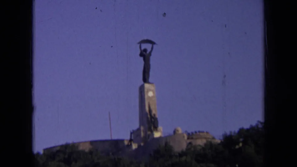 Distant Russia landmark view on 8mm film, with the statue centered above trees and a dark film-frame edge.