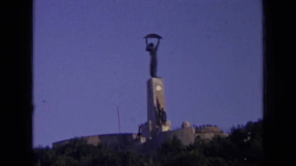 Final 8mm frame holds on the distant Soviet-era public monument in Russia, with trees and low structures below.