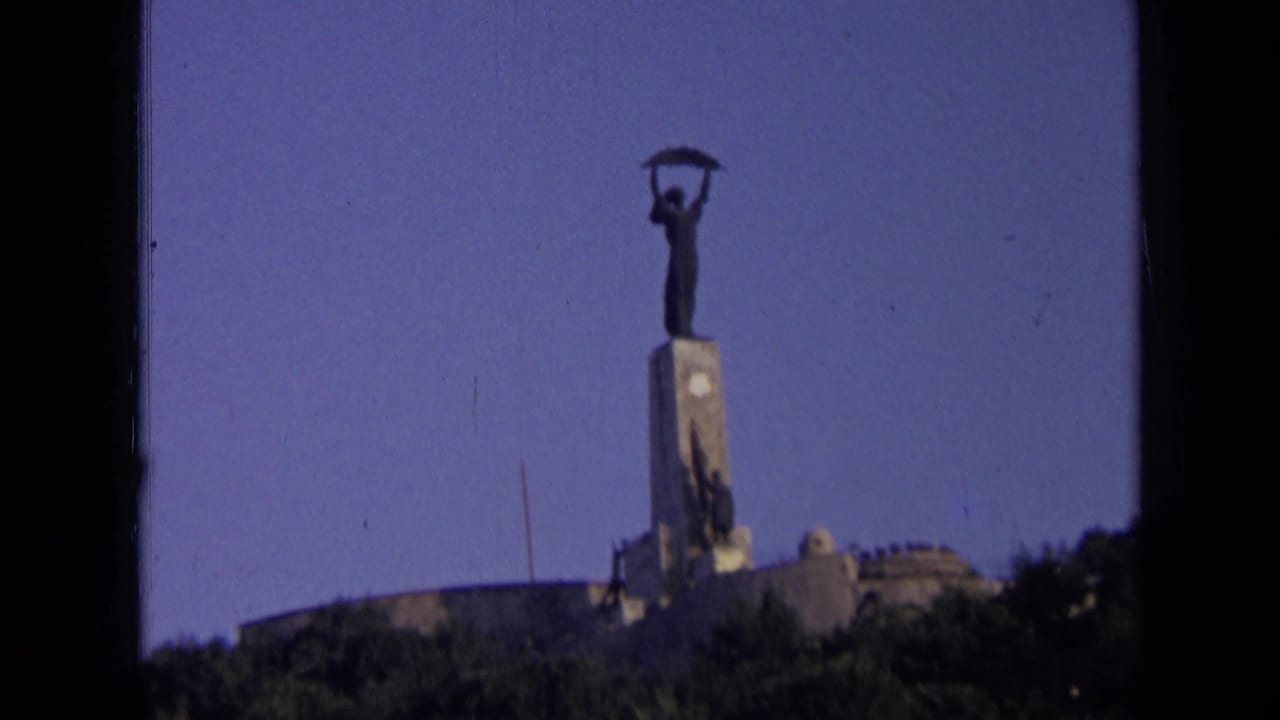 1963 Russia 8mm frame showing a distant Soviet-era style statue holding a sickle above a tall pedestal, with trees below.