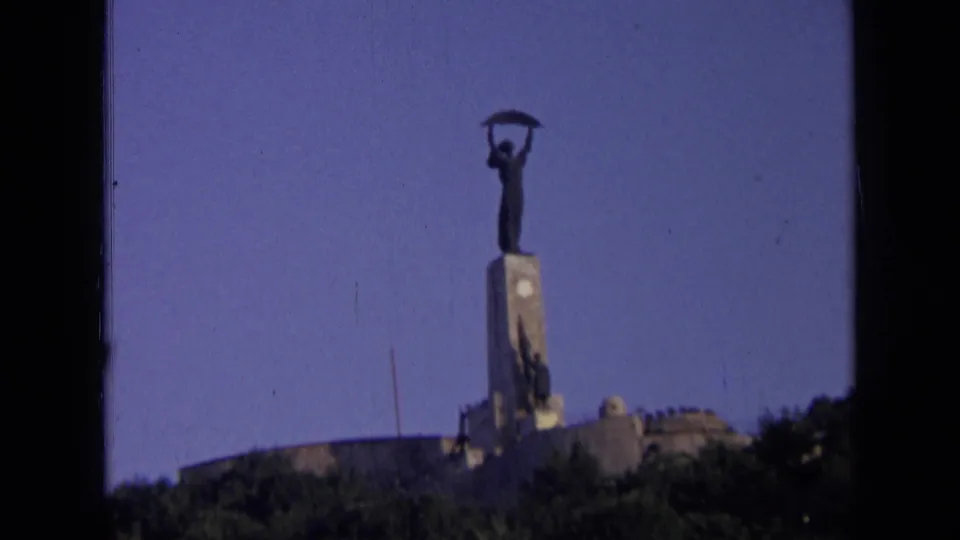 1963 Russia 8mm frame showing a distant Soviet-era style statue holding a sickle above a tall pedestal, with trees below.