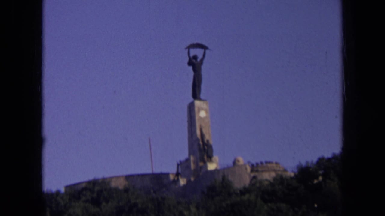 The 8mm frame holds on the same Russian monument, with the statue silhouetted above its pedestal and greenery at the base.