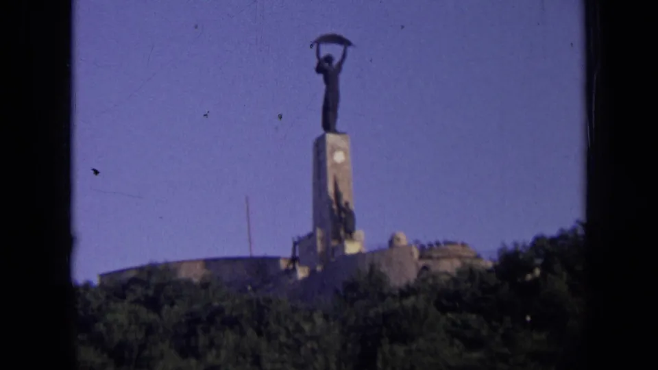 Final 8mm frame shows the Russian monument from below, with the sickle-bearing statue above the pedestal and dark trees across the bottom.