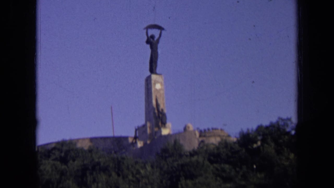 Distant 8mm view of a Russian hillside monument, with the statue silhouetted against a clear blue sky.
