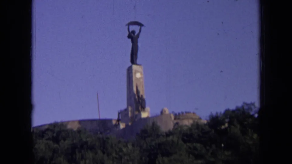 Distant 8mm view of a Russian hillside monument, with the statue silhouetted against a clear blue sky.