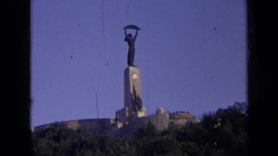 Vintage 8mm frame of the hillside monument in Russia, showing the pedestal and figure through soft focus and film grain.