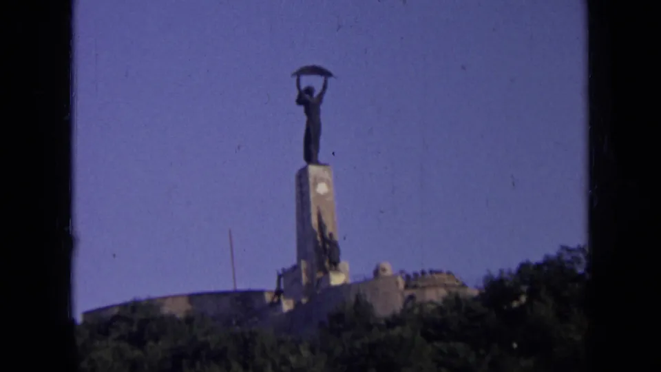 1963 Russia frame with soft focus and grain showing a distant monumental figure on a pedestal above a tree-lined foreground.